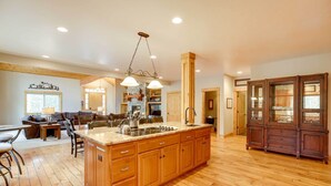 A spacious kitchen with wooden cabinets, a large island, and a dining area with a sofa and chairs. - Sunriver Group Getaway: Explore Deschutes Forest! (Bend)