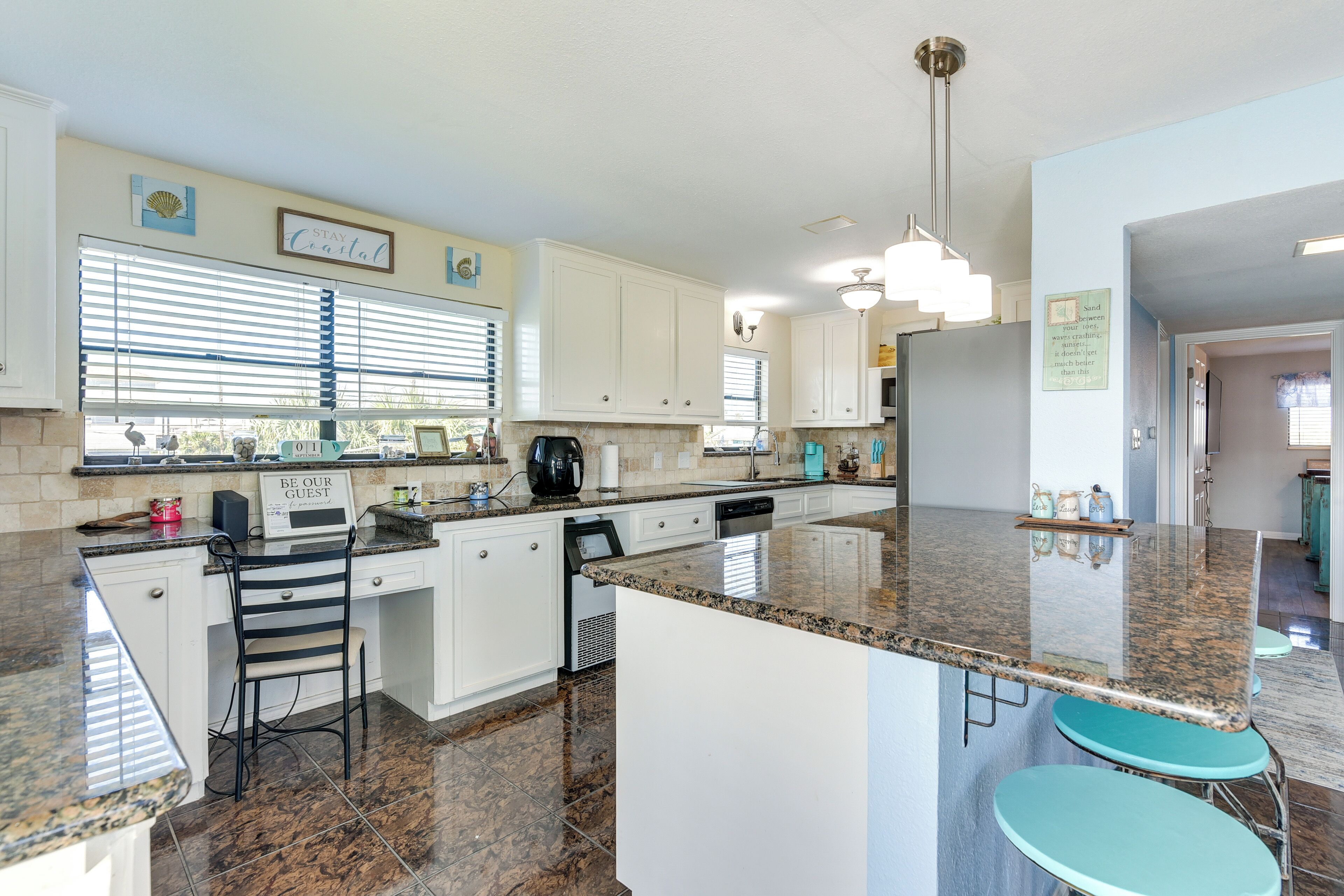 A spacious kitchen with white cabinets, granite countertops, and a central island with bar stools.
