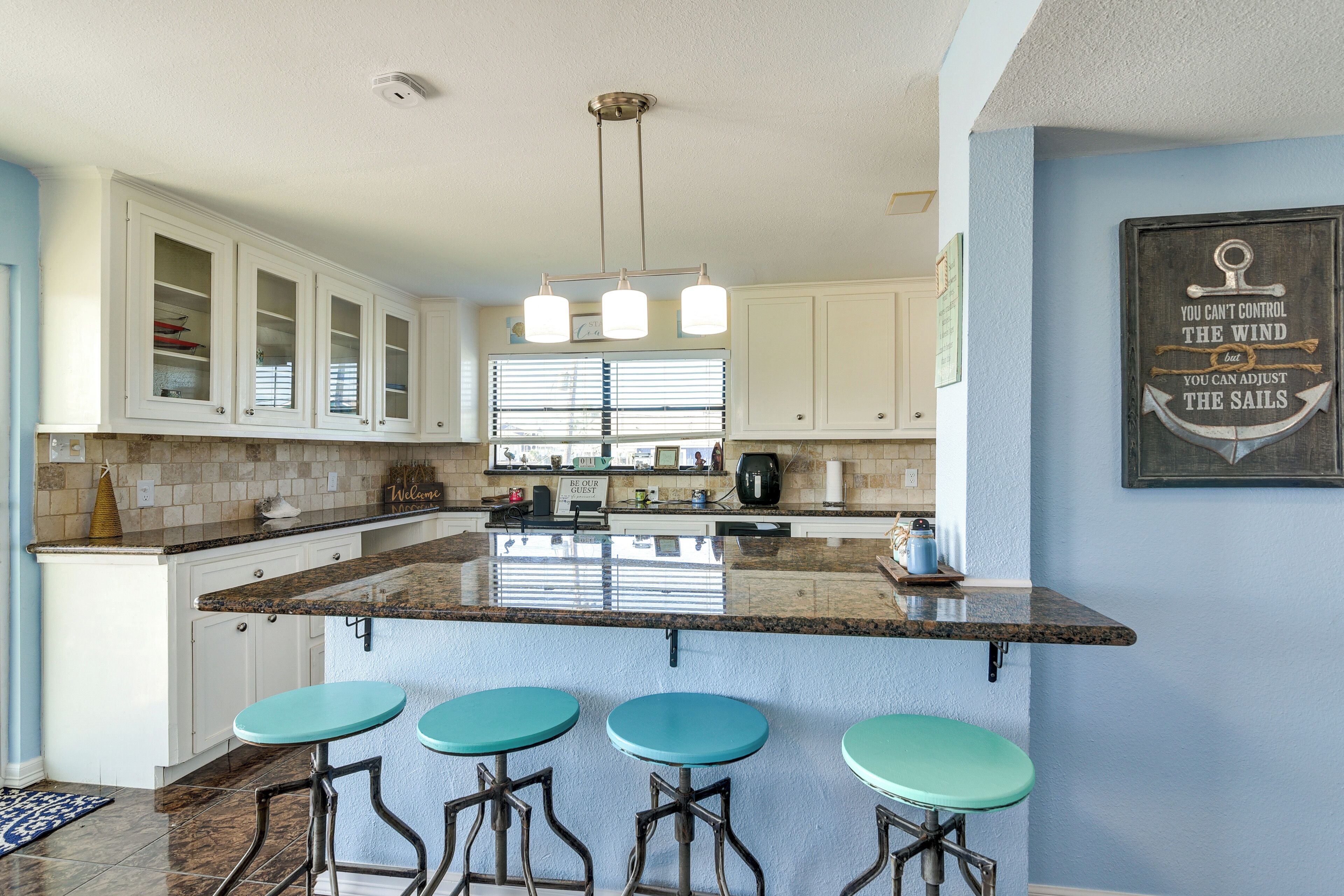 A kitchen with white cabinets, a granite countertop, and three teal bar stools.