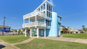 A two-story building with a balcony on the upper floor, a covered porch on the ground floor, and a clear blue sky in the background. - Walk to Beach: Family-friendly Galveston Home! (Galveston)