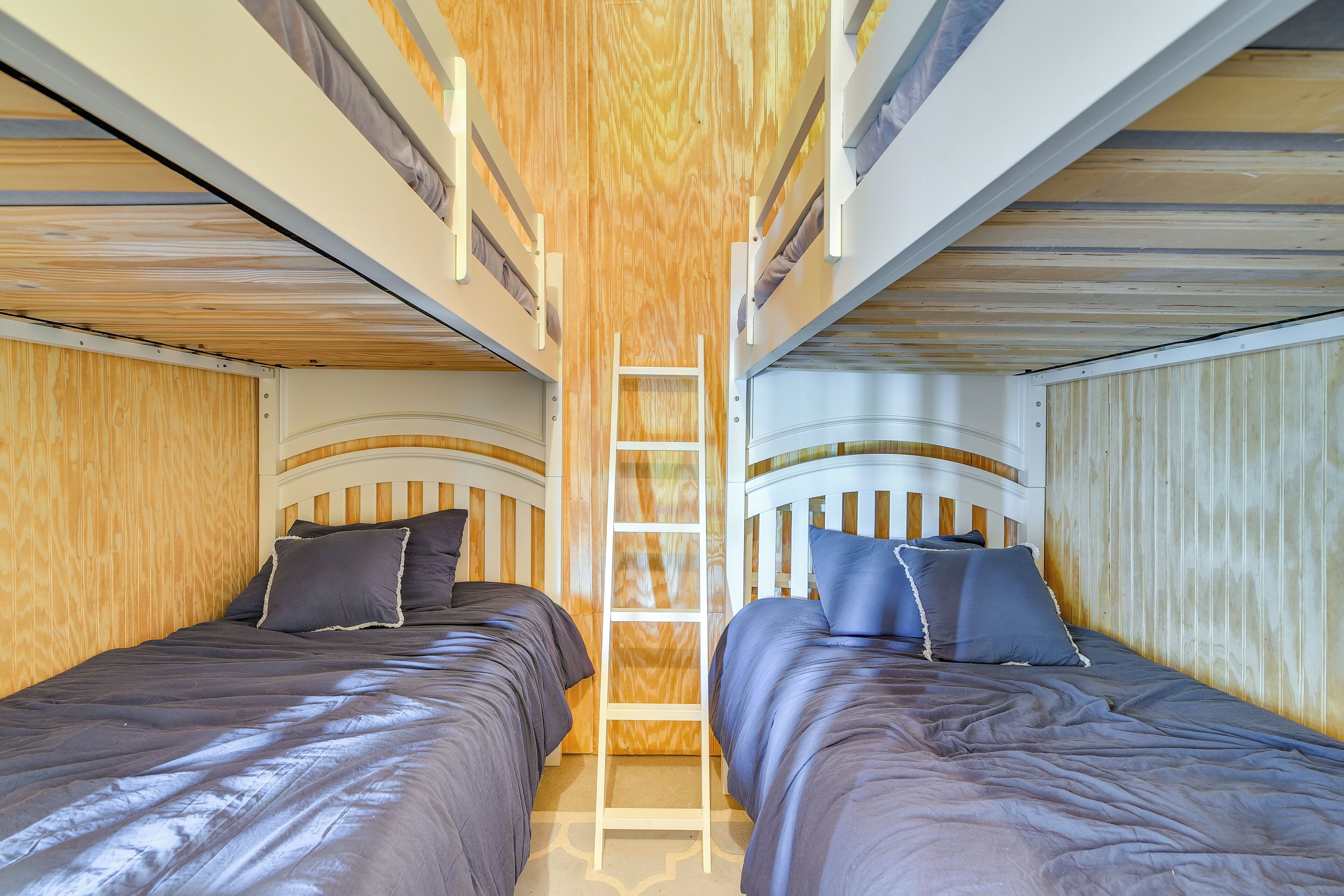 A bunk bed room with a ladder, wooden walls, and two beds with dark bedding.