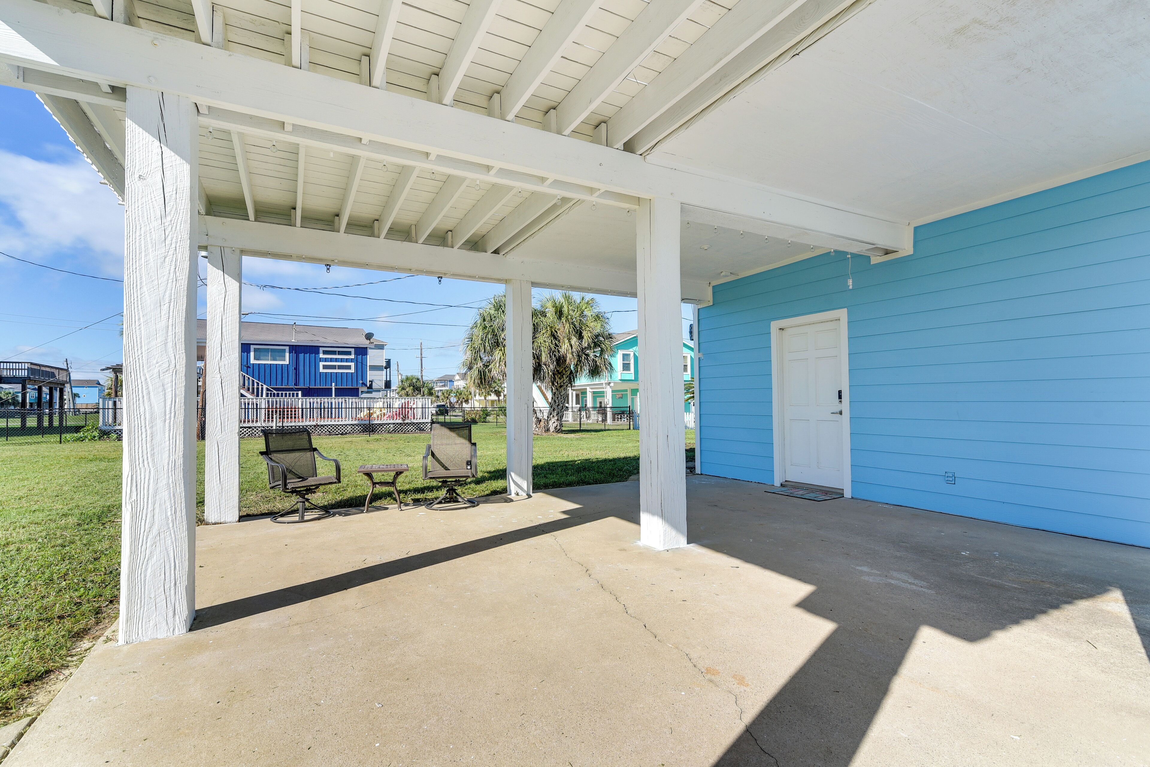 A covered outdoor area with a concrete floor, white columns, and a blue building in the background.