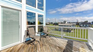 A wooden deck with two chairs and a glass door, overlooking a grassy yard and neighboring houses. - Walk to Beach: Family-friendly Galveston Home! (Galveston)