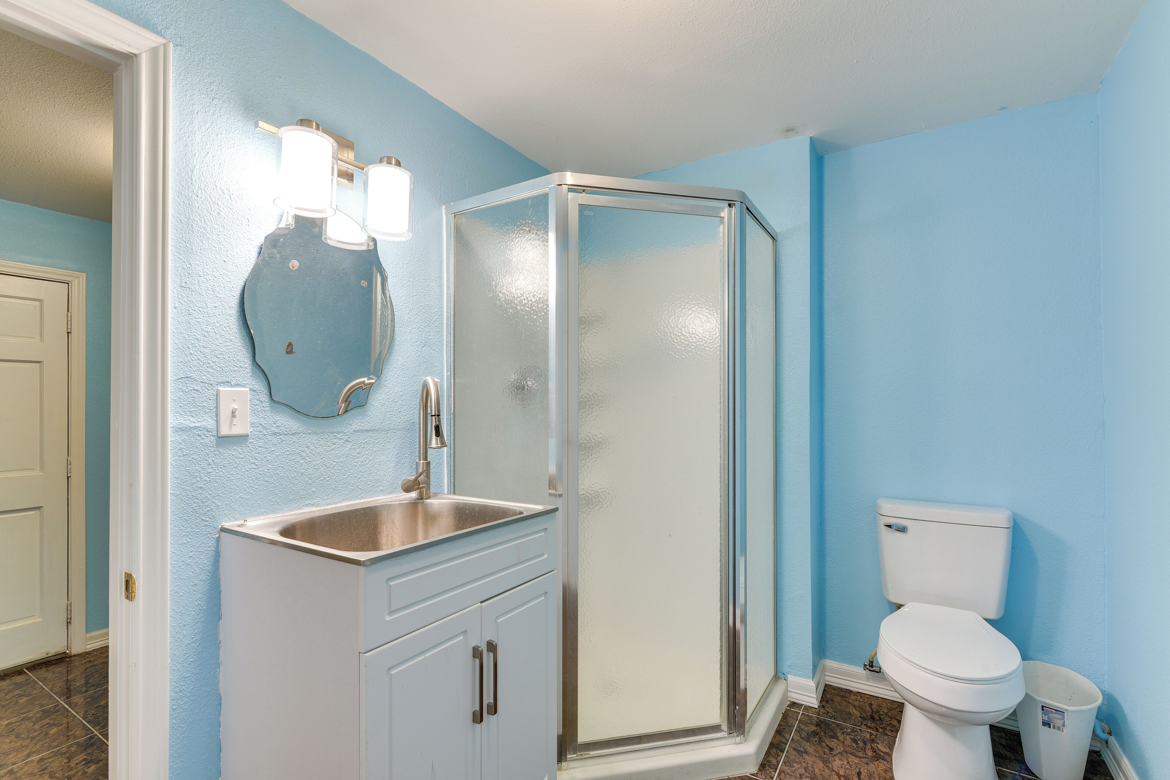 Un baño con ducha envuelta en vidrio, inodoro blanco y lavamanos con espejo.