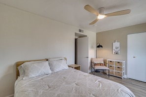 A bedroom with a bed, a ceiling fan, a nightstand, a chair, a lamp, and a storage unit.