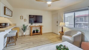 Un salon moderne doté d’un téléviseur à écran plat, de meubles en bois, d’un ventilateur de plafond et d’une grande fenêtre.