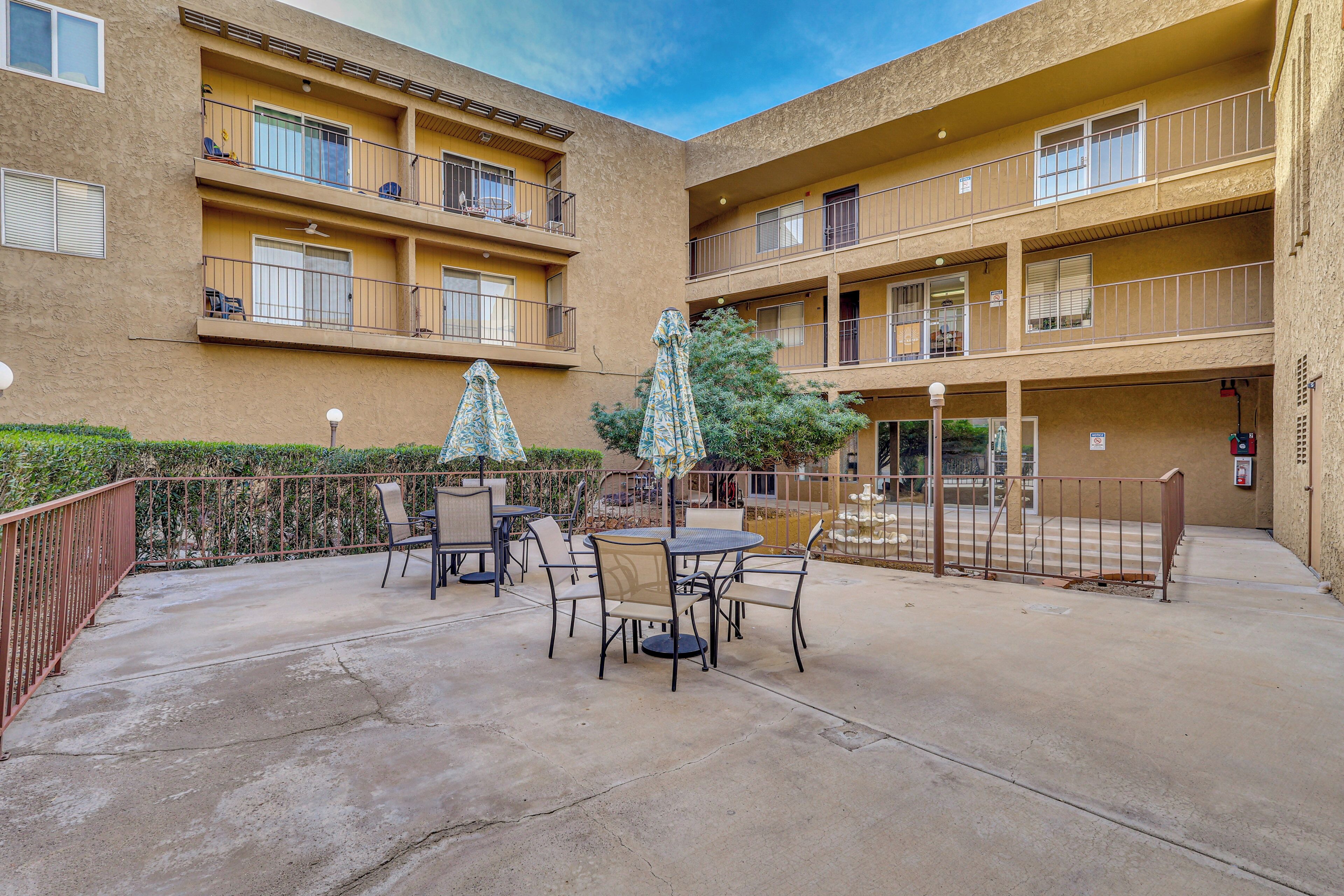 Un patio con mobiliario exterior, un árbol y un edificio con varios balcones.