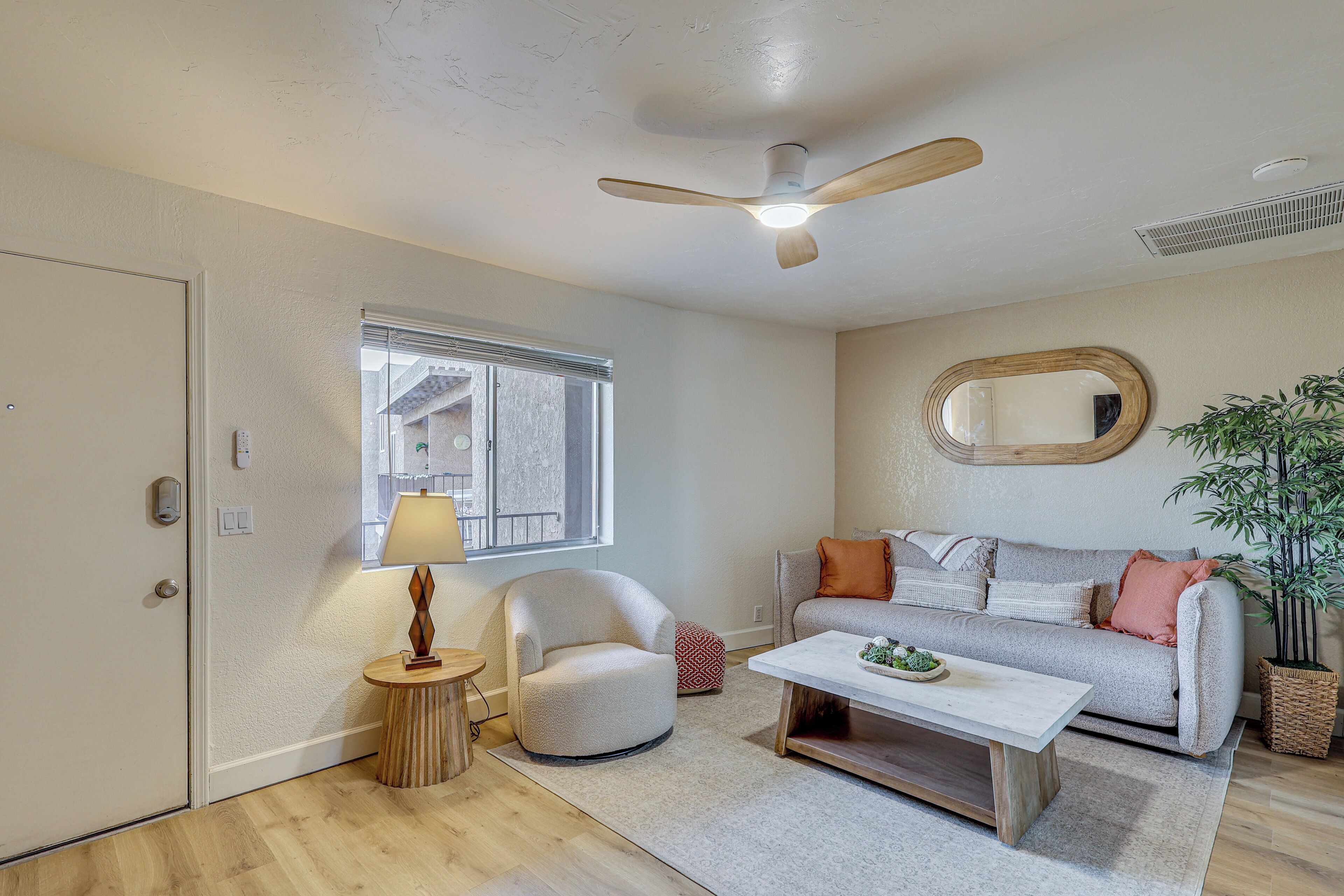 Un salon avec un ventilateur de plafond, un canapé, une table basse, une lampe et une fenêtre.