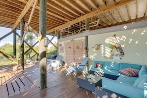 A covered outdoor seating area with wooden flooring, a blue sofa, and striped cushions.