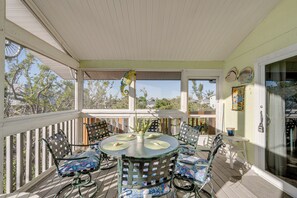 A covered outdoor patio with a round table and chairs, a potted plant, and a view of trees and buildings in the background.