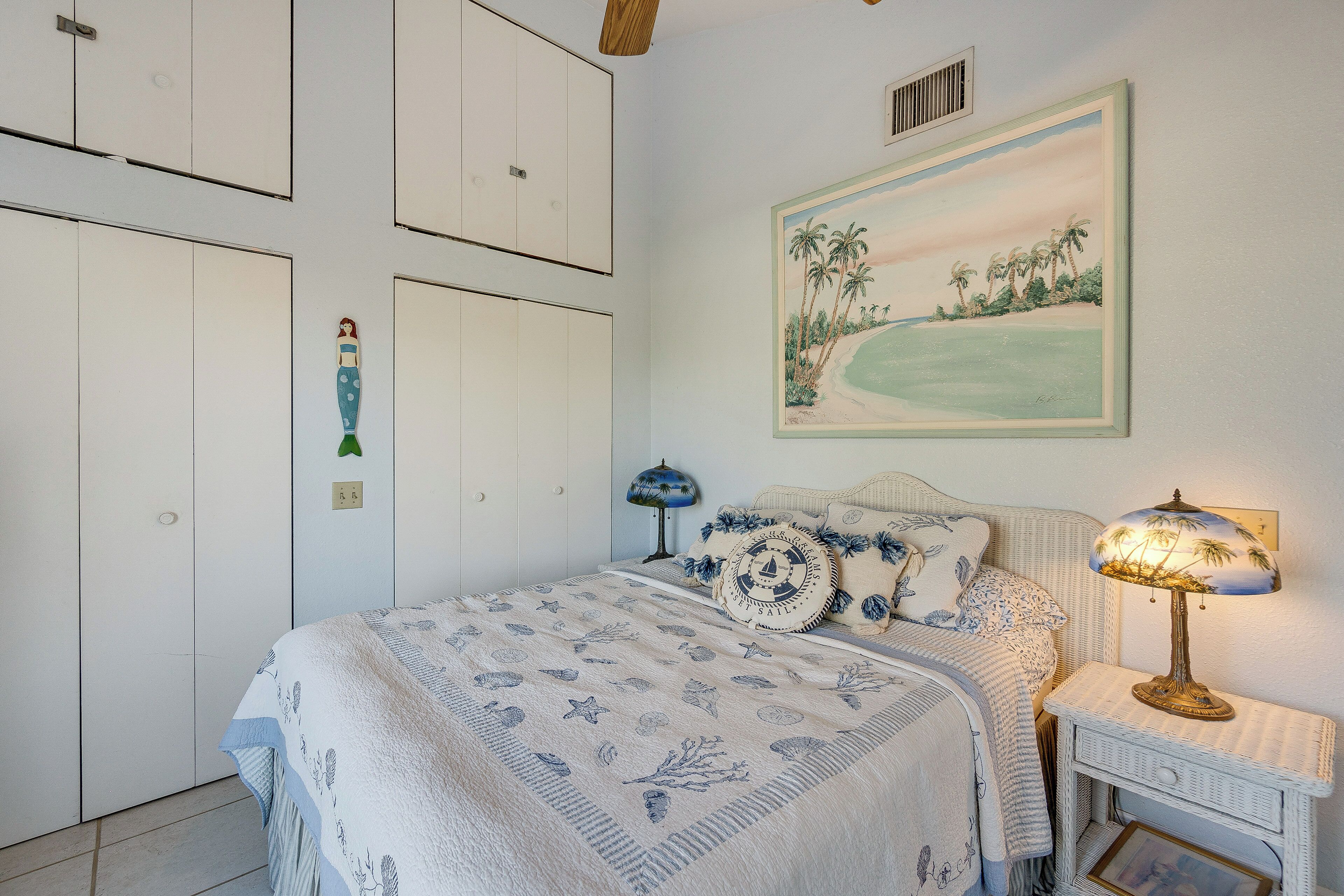 A bedroom with a bed, a nightstand, a lamp, a painting, and a wardrobe.