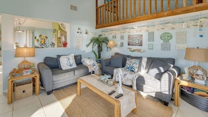 A cozy living room with two grey sofas, a wooden coffee table, and a staircase with wooden railings.