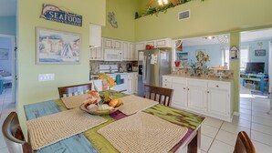 A kitchen with white cabinets, a microwave, and a refrigerator. There is a dining table with placemats and a centerpiece.