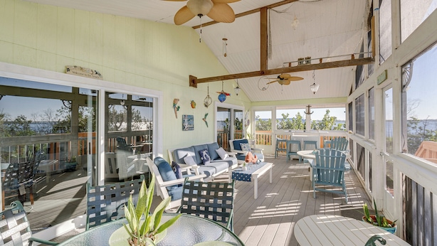 A covered outdoor deck with seating, a ceiling fan, and large windows offering views of the outdoors.