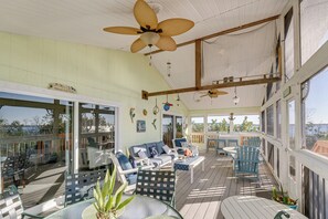 A covered outdoor deck with seating, a ceiling fan, and large windows offering views of the outdoors. - Little Gasparilla Island Paradise: Walk to Beach! (Placida)