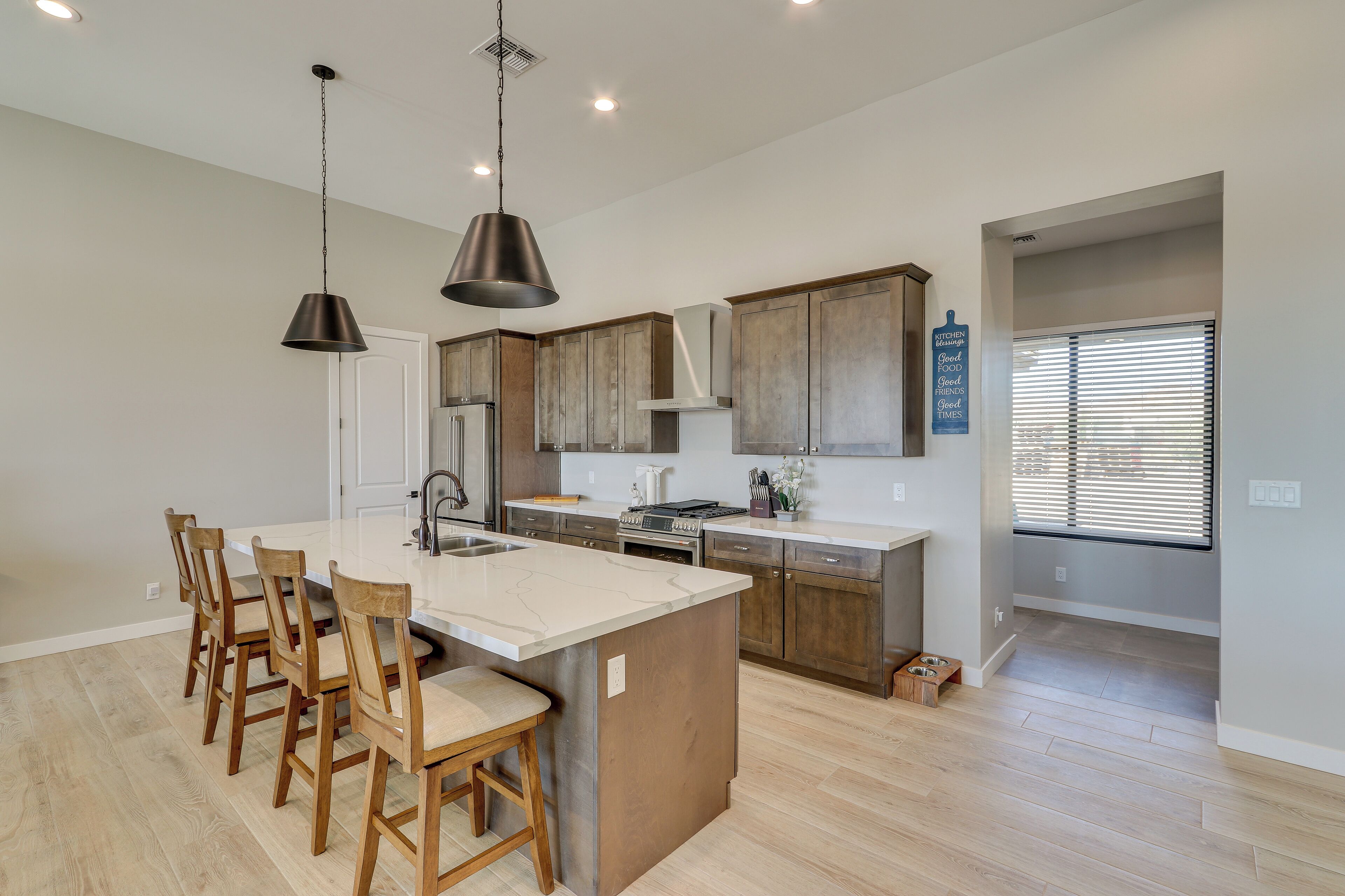 A modern kitchen with a large island, wooden chairs, pendant lights, and a view to the living area.