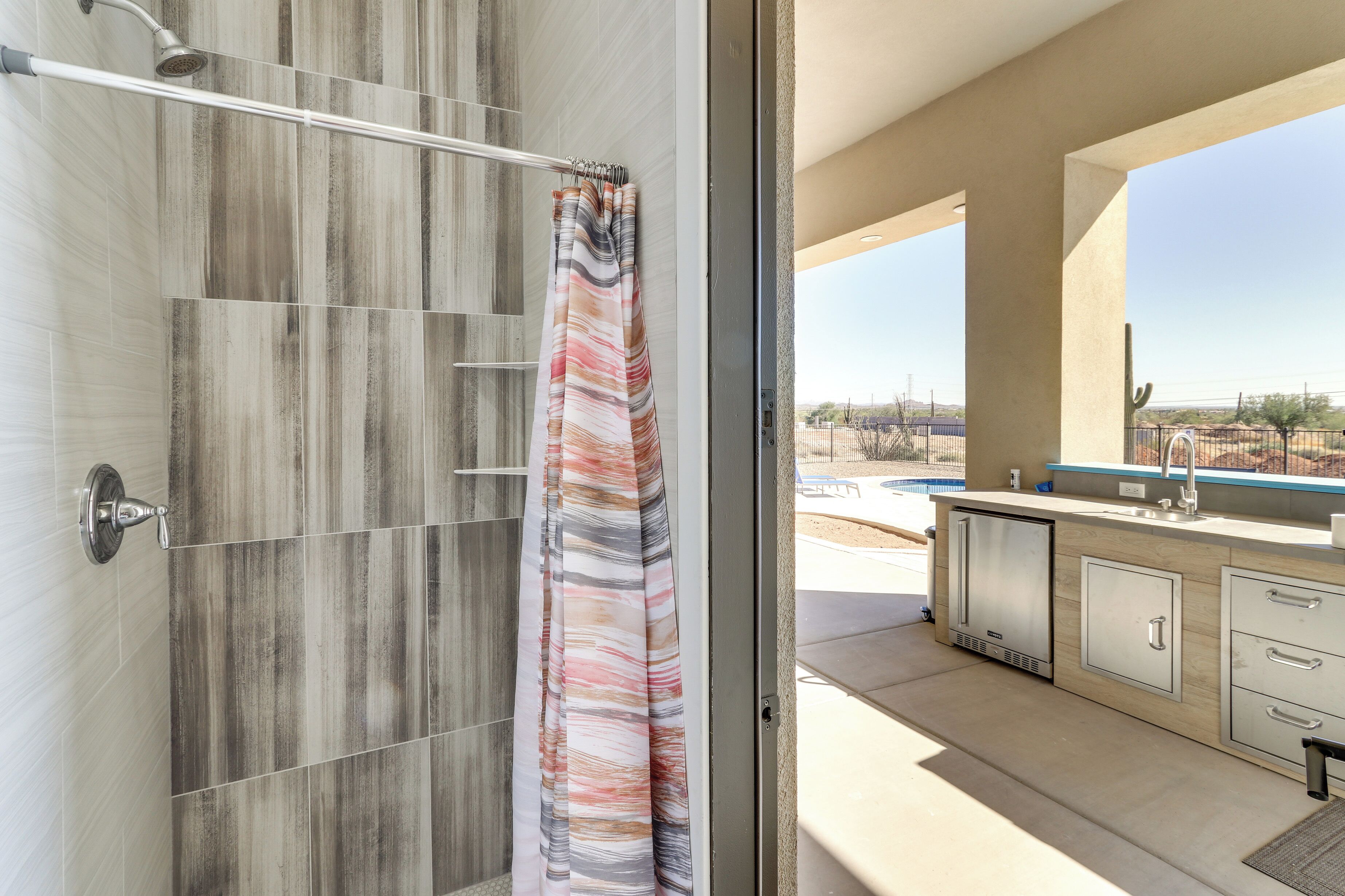 A modern bathroom with a shower, a curtain, and a view of a pool and outdoor area.