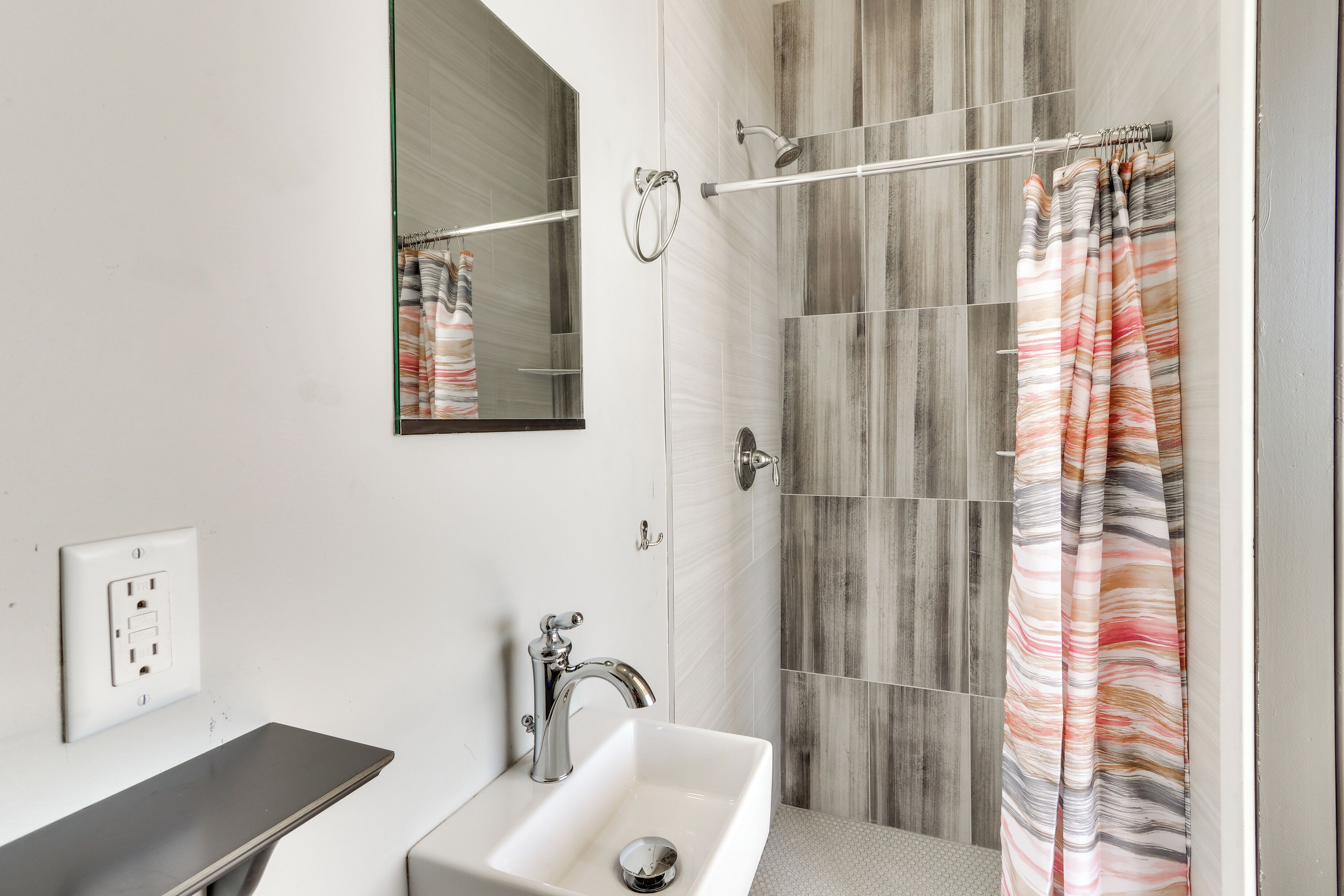 Une salle de bain avec un lavabo blanc, un miroir, une douche avec un rideau à rayures et un mur carrelé.