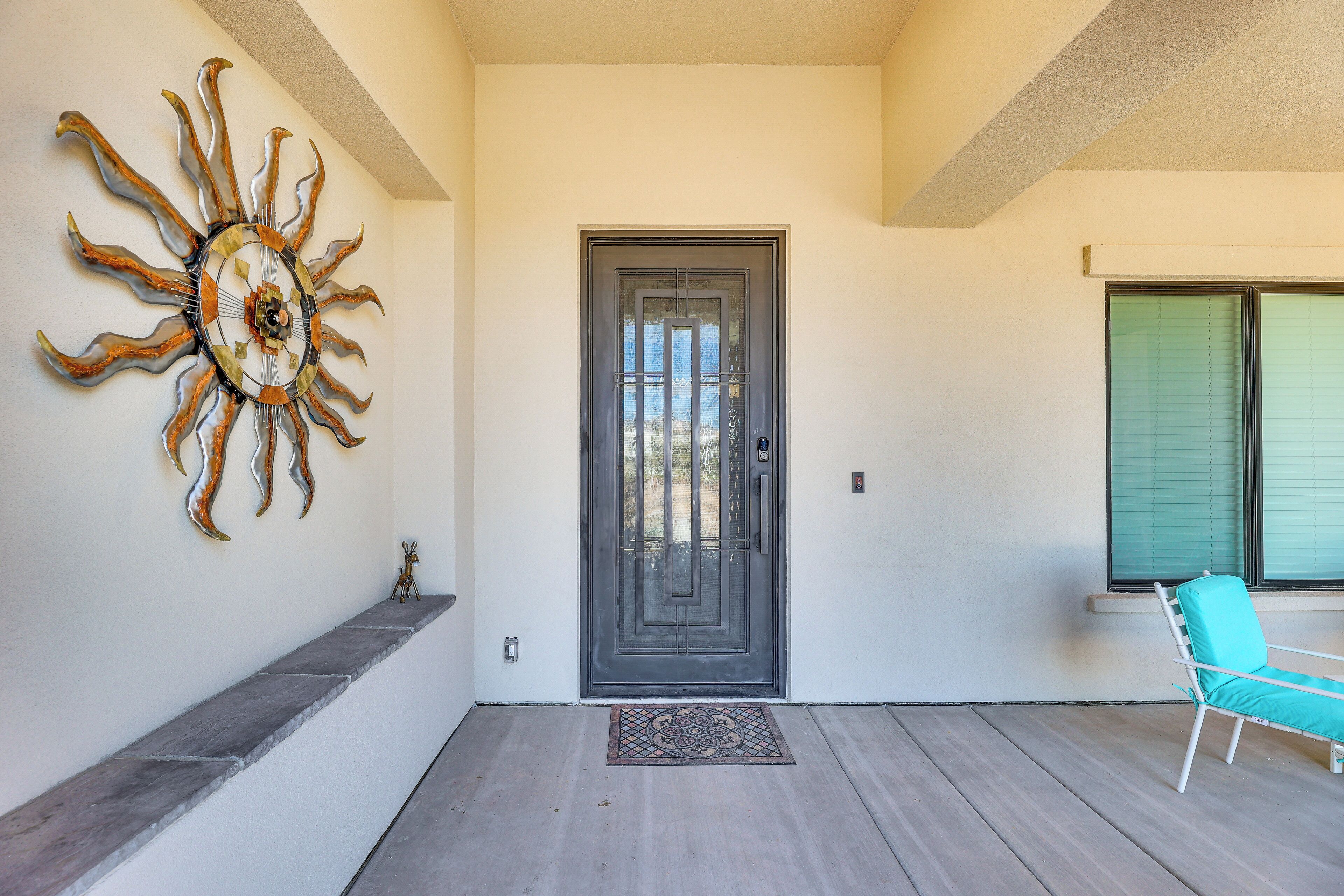 A modern entrance with a sunburst wall art, a dark door, and a teal chair by a window.