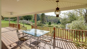 Eine überdachte Terrasse mit einem Glastisch und Metallstühlen, mit Blick auf einen üppigen Garten und Bäume.