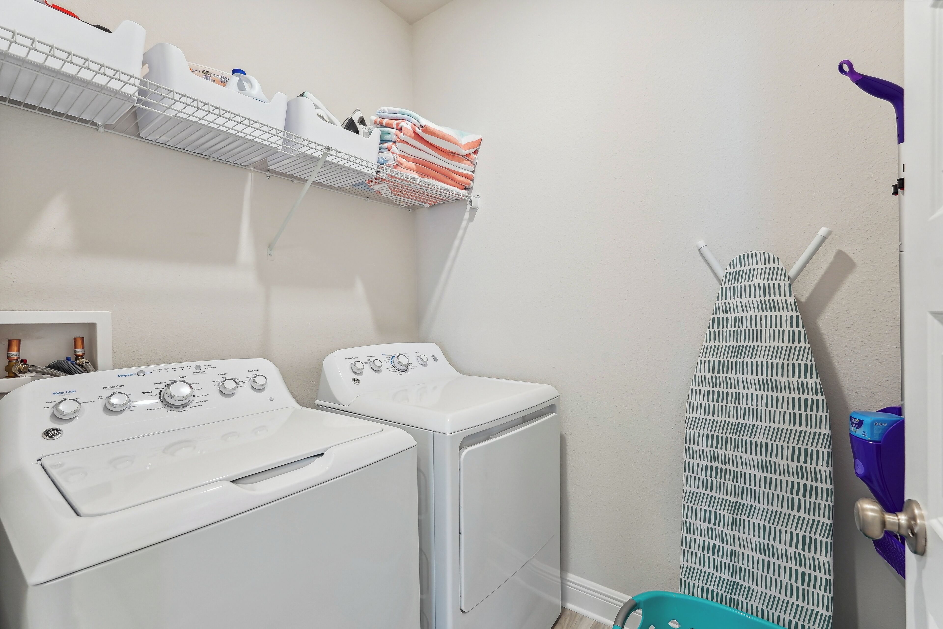 Un espace buanderie comprenant deux machines à laver blanches, un étendoir et une étagère avec des serviettes pliées et du matériel de lessive.