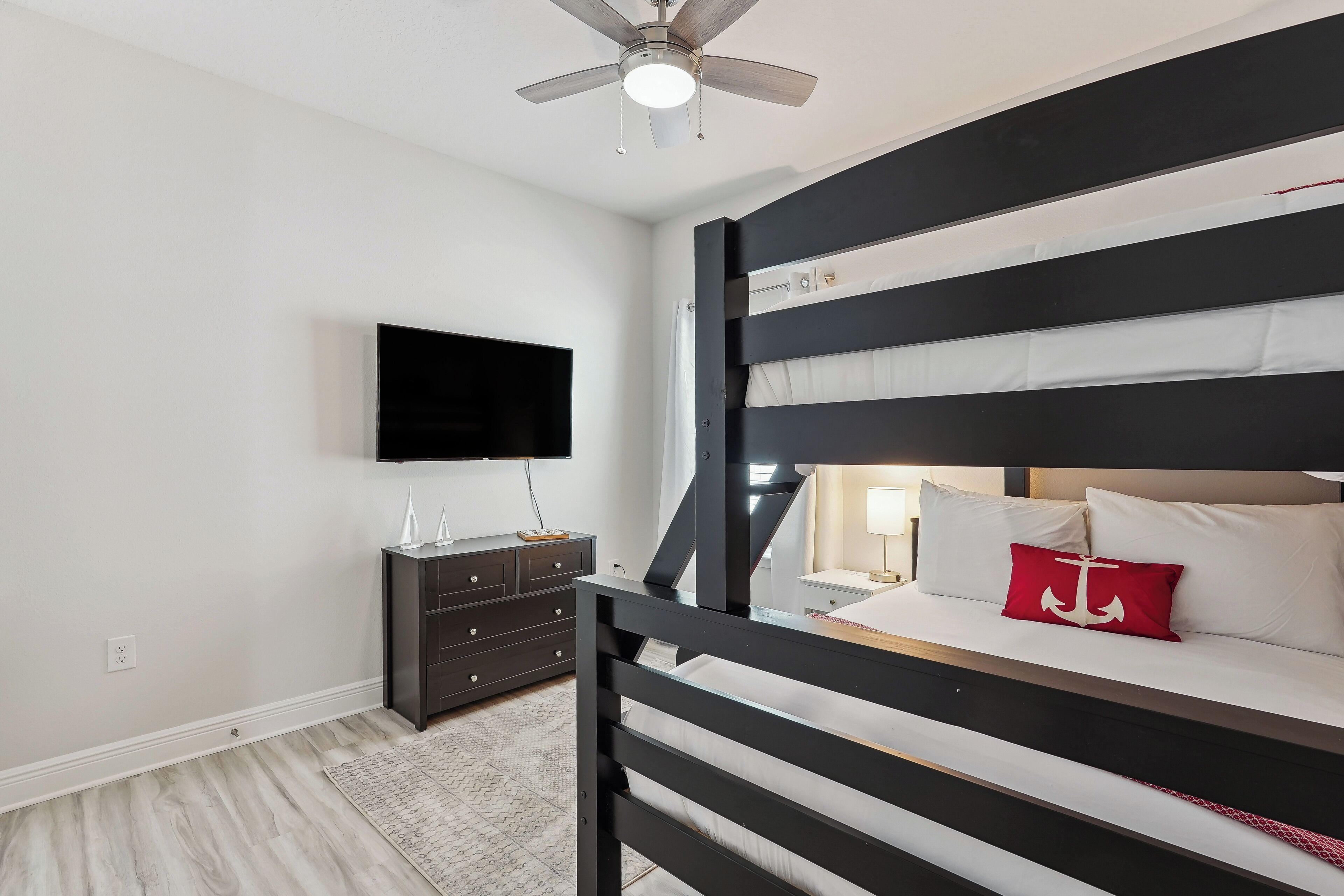 A bedroom with a bunk bed, a flat-screen TV, a dark wooden dresser, and a ceiling fan.