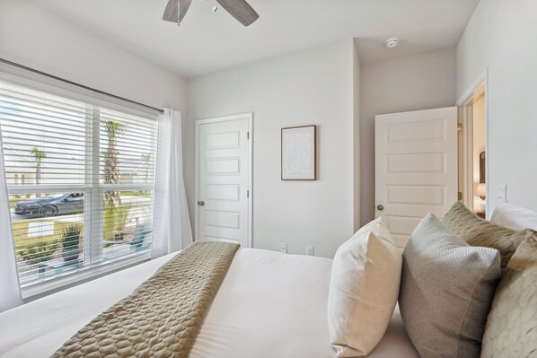 Quarto com cama grande, paredes brancas e janela com persianas.