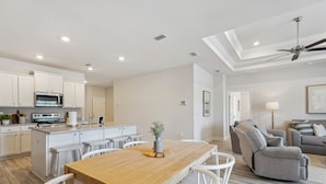 Una cocina moderna con armarios blancos, una isla central y un comedor con mesa de madera y sillas blancas.