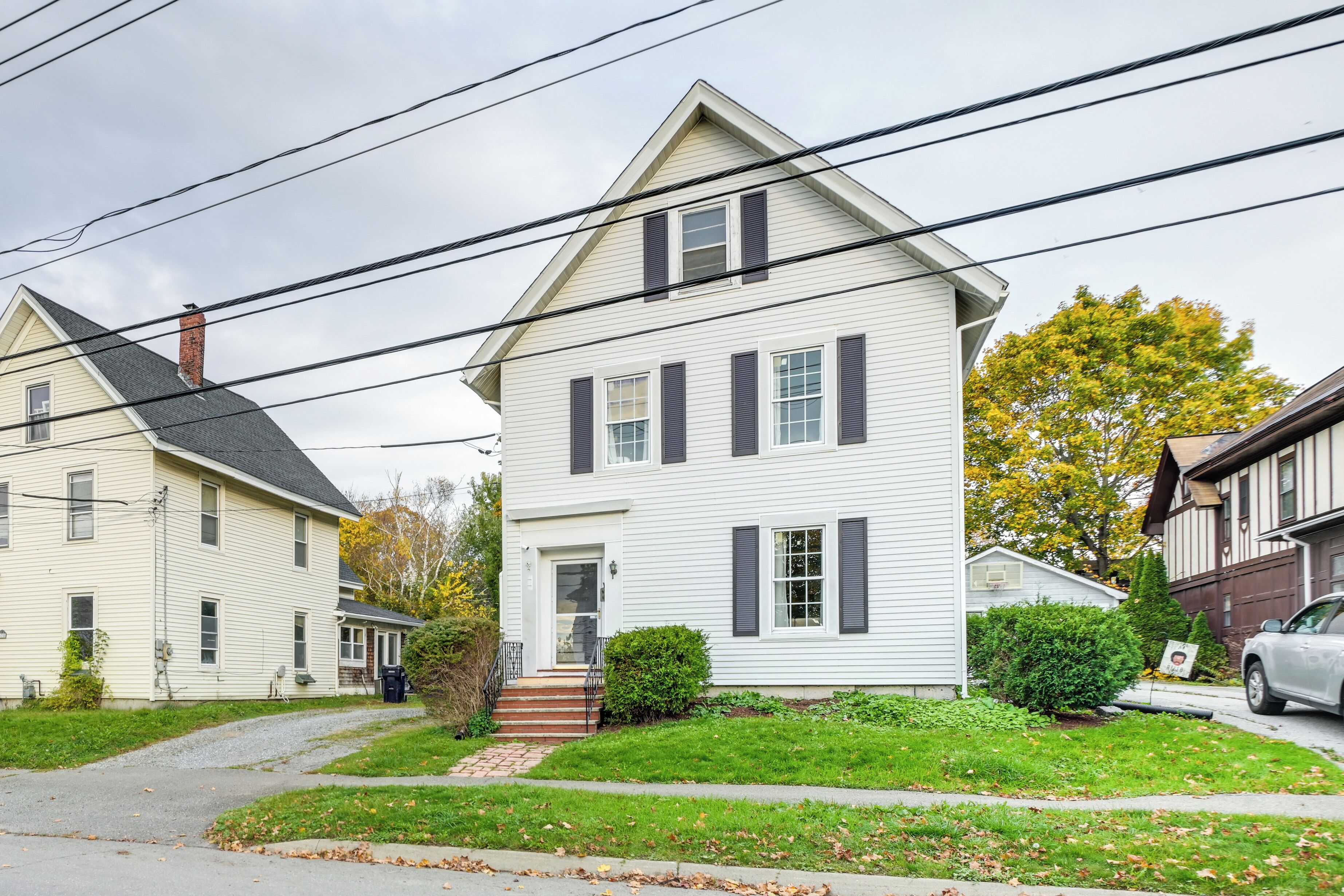 A two-story house with a front porch, a chimney, and a small front yard with a hedge.