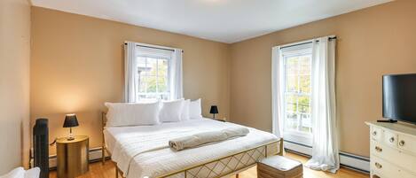 A bedroom with a bed, bedside tables, a TV, and a window with curtains.