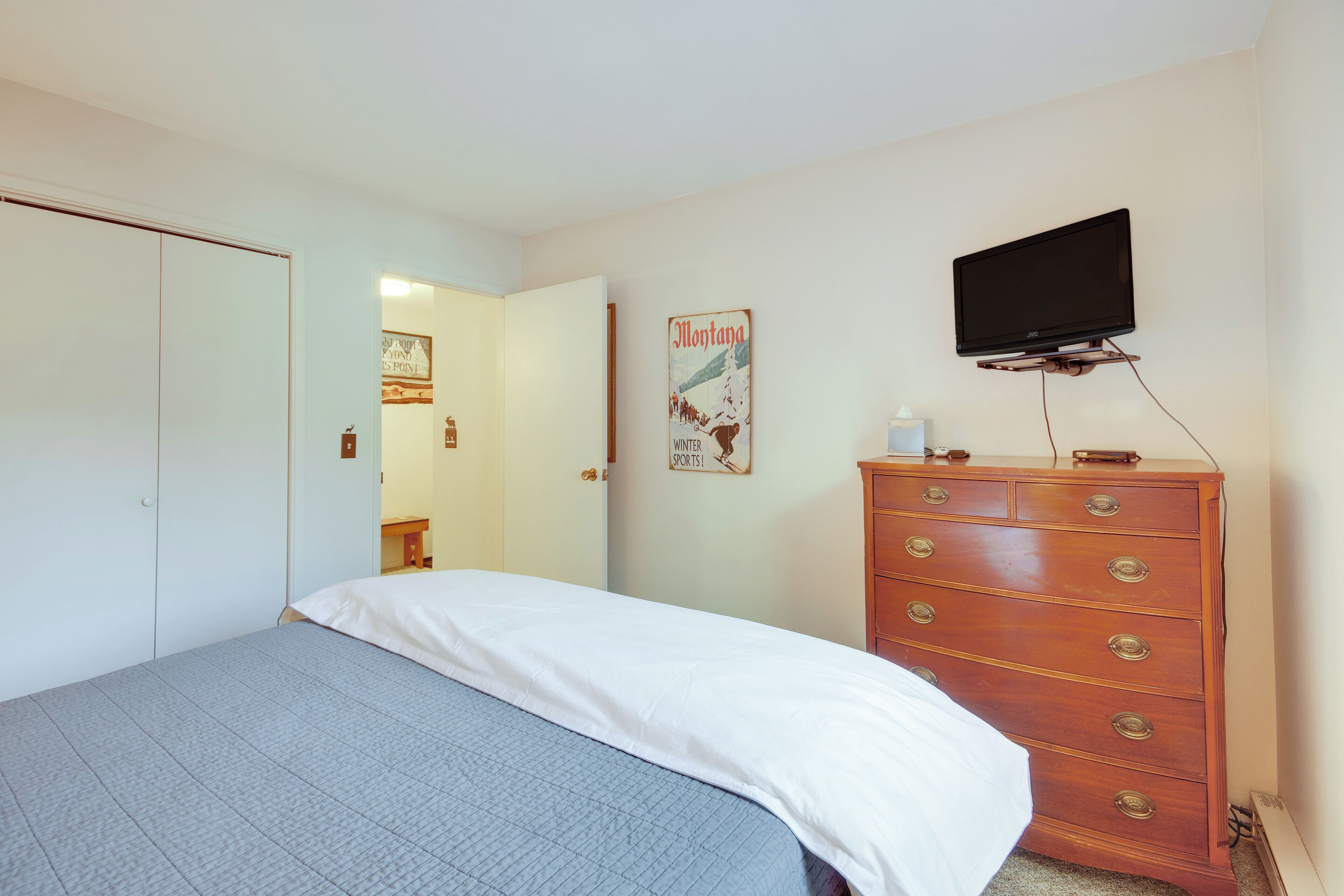 Een slaapkamer met een bed, een kaptafel, een televisie en een deur die naar een andere kamer leidt.