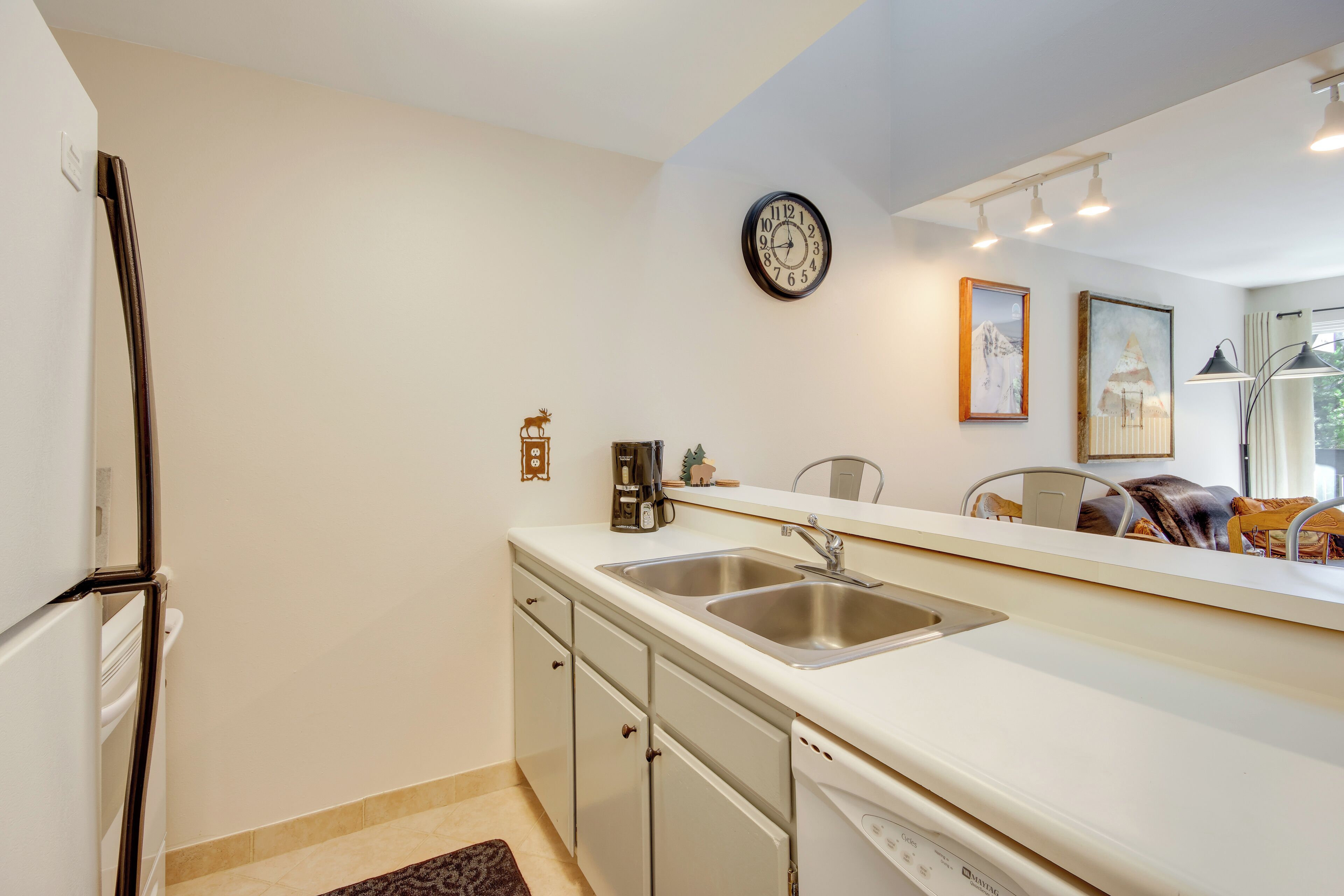 A kitchen with a refrigerator, double sink, and a clock on the wall.