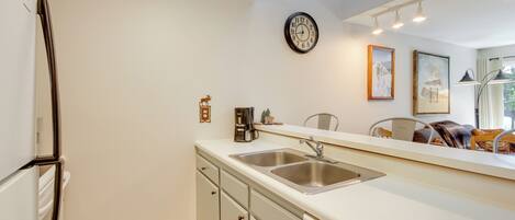 A kitchen with a refrigerator, double sink, and a clock on the wall.
