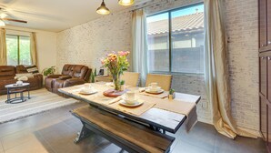A dining area with a long table set for four, a sofa, and a ceiling fan. - Luxe Family Home w/ Pool, 13 Mi to Dtwn Phoenix! (Laveen)