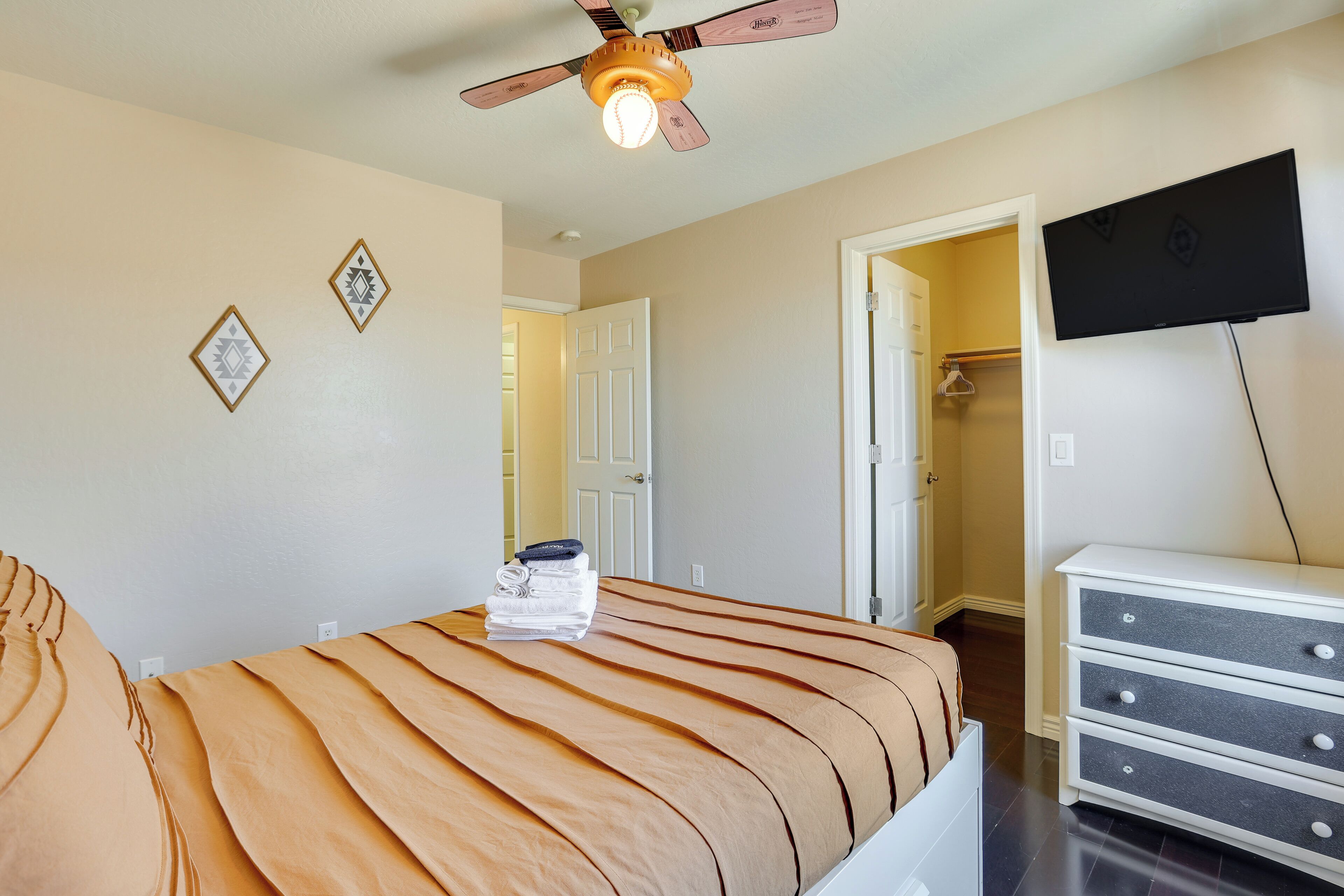 A bedroom with a bed, a ceiling fan, a TV, and a dresser.