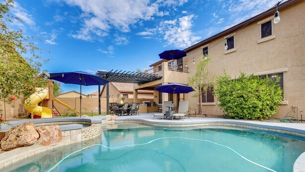A swimming pool with a slide, outdoor furniture, and umbrellas. - Luxe Family Home w/ Pool, 13 Mi to Dtwn Phoenix! (Laveen)