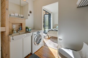 A compact, modern bathroom with a built-in washing machine, a mirror, and a shelf with towels. - Secluded Bryson City Tiny Cabin Near River Access! (Bryson City)