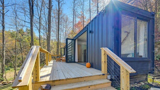 A modern cabin with a wooden deck, a glass door entrance, and a view of the surrounding forest. - Bryson City Tiny Cabin w/ Deck Near River Access! (Bryson City)