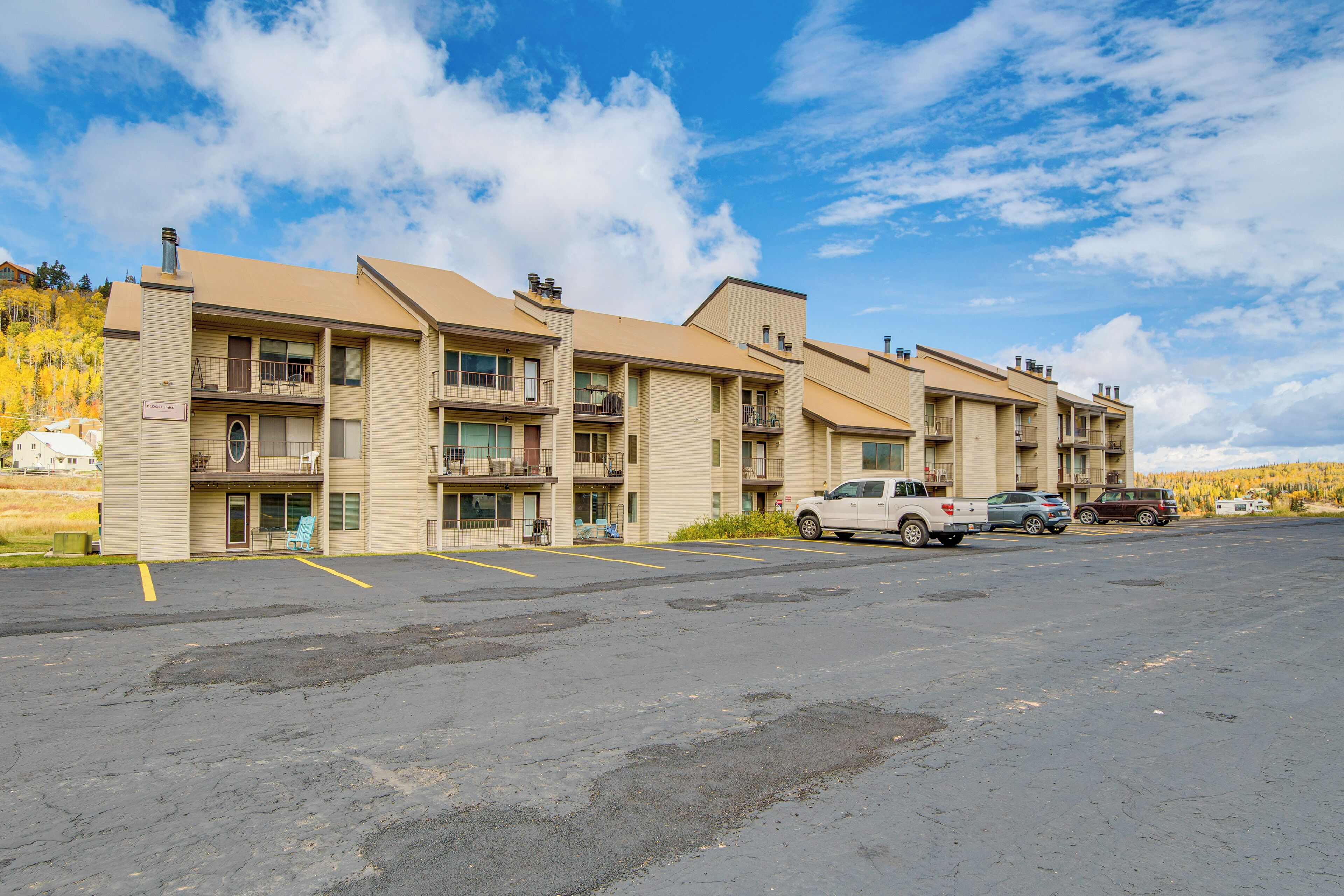 Un motel à plusieurs étages avec un parking, plusieurs véhicules stationnés et un ciel dégagé.