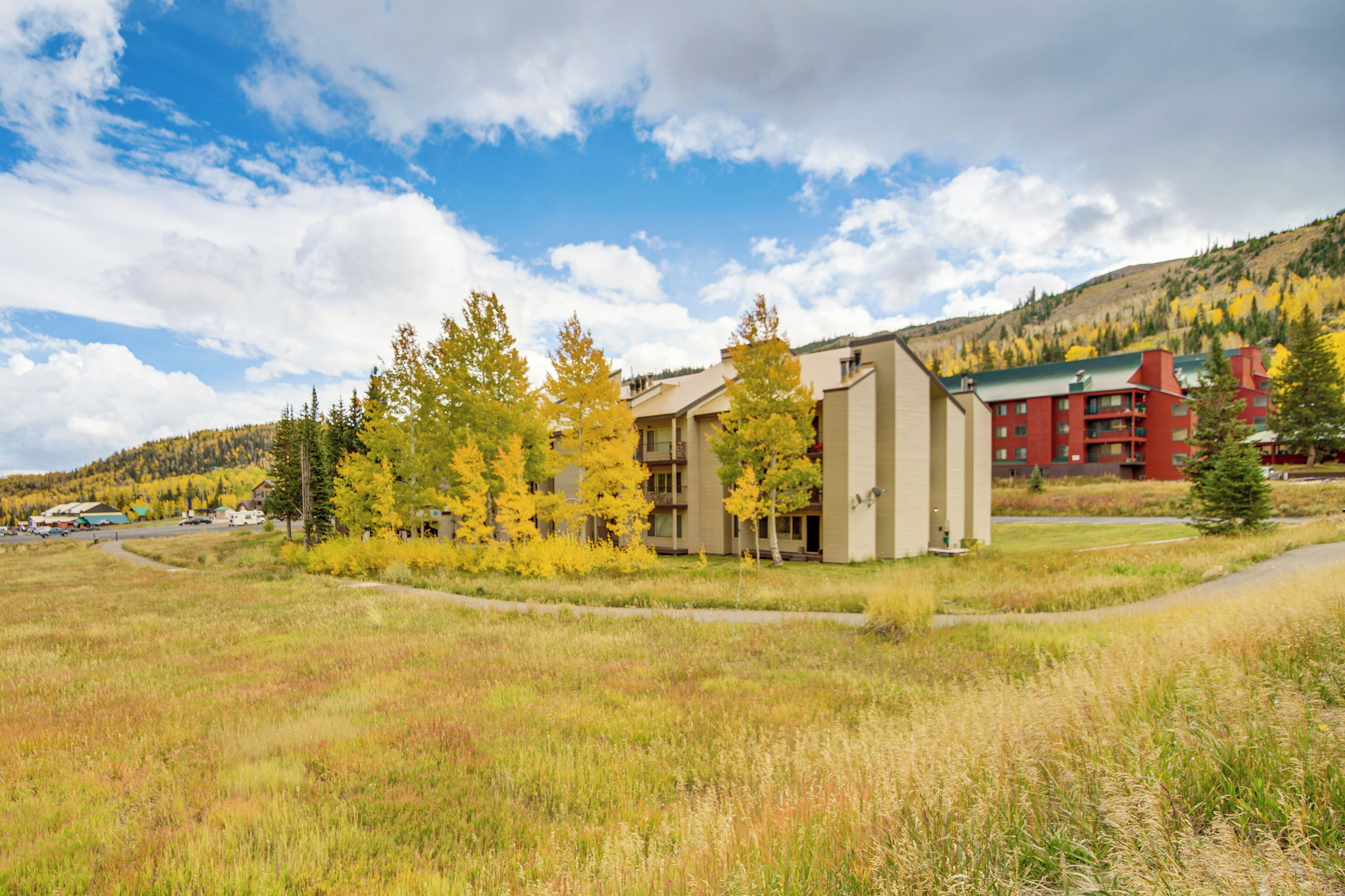 A modern building with a flat roof, surrounded by a grassy field and trees with yellow leaves.