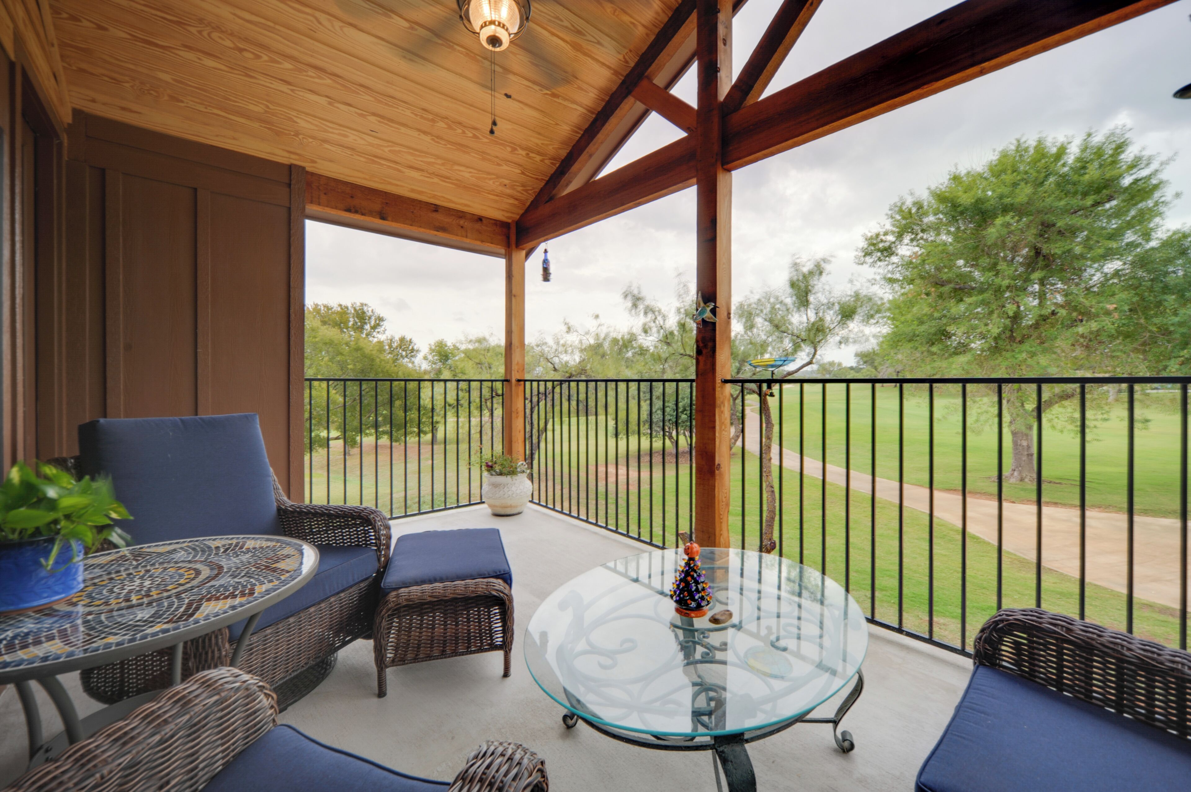 A covered outdoor seating area with wicker furniture, a glass table, and a view of a golf course.
