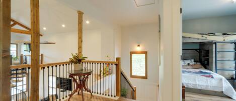 A spacious room with a wooden staircase, a small table with a vase, and a bed with a white comforter.