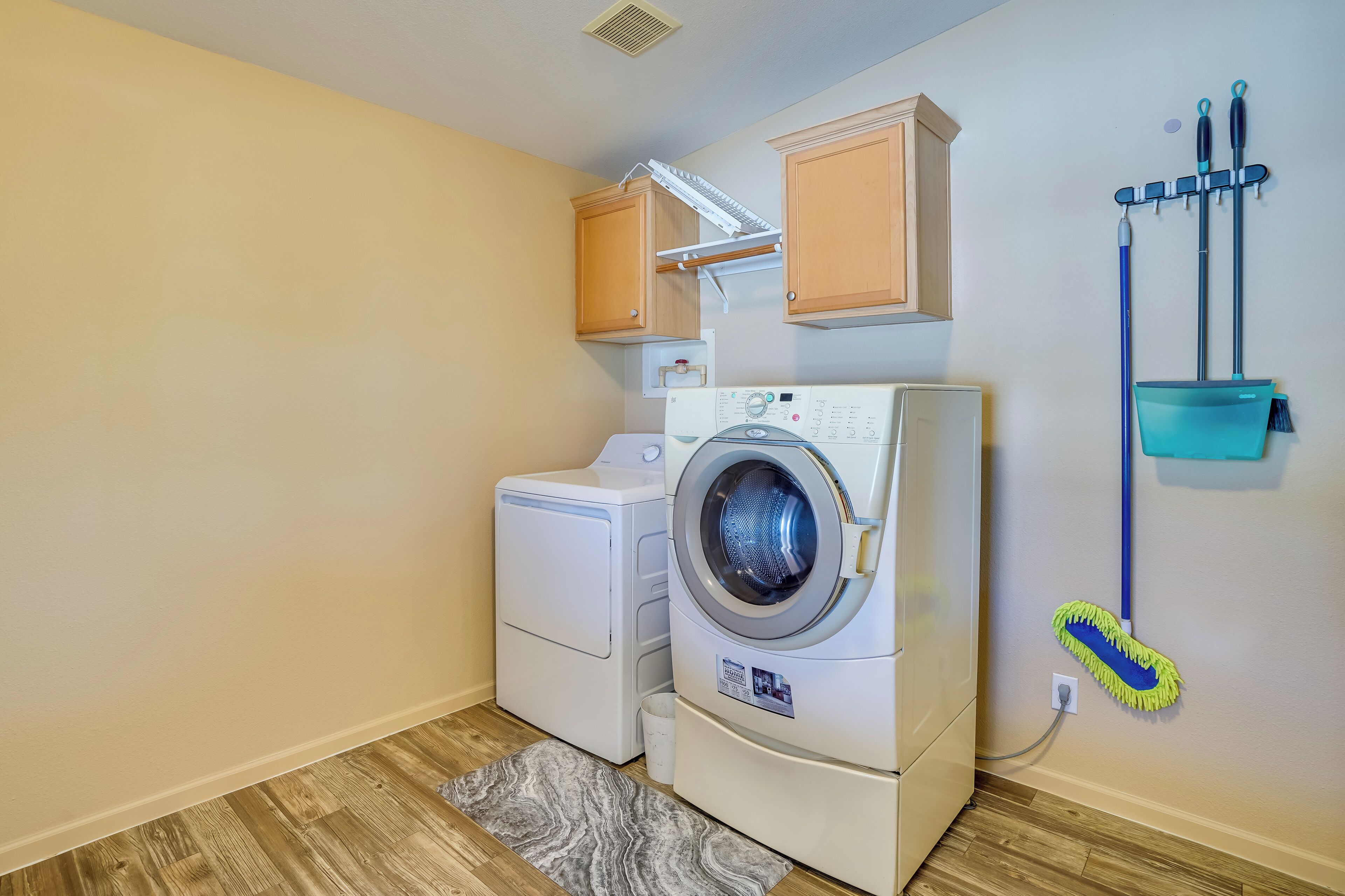 A laundry area with a front-loading washer and dryer, wooden cabinets, a mop, and a broom.