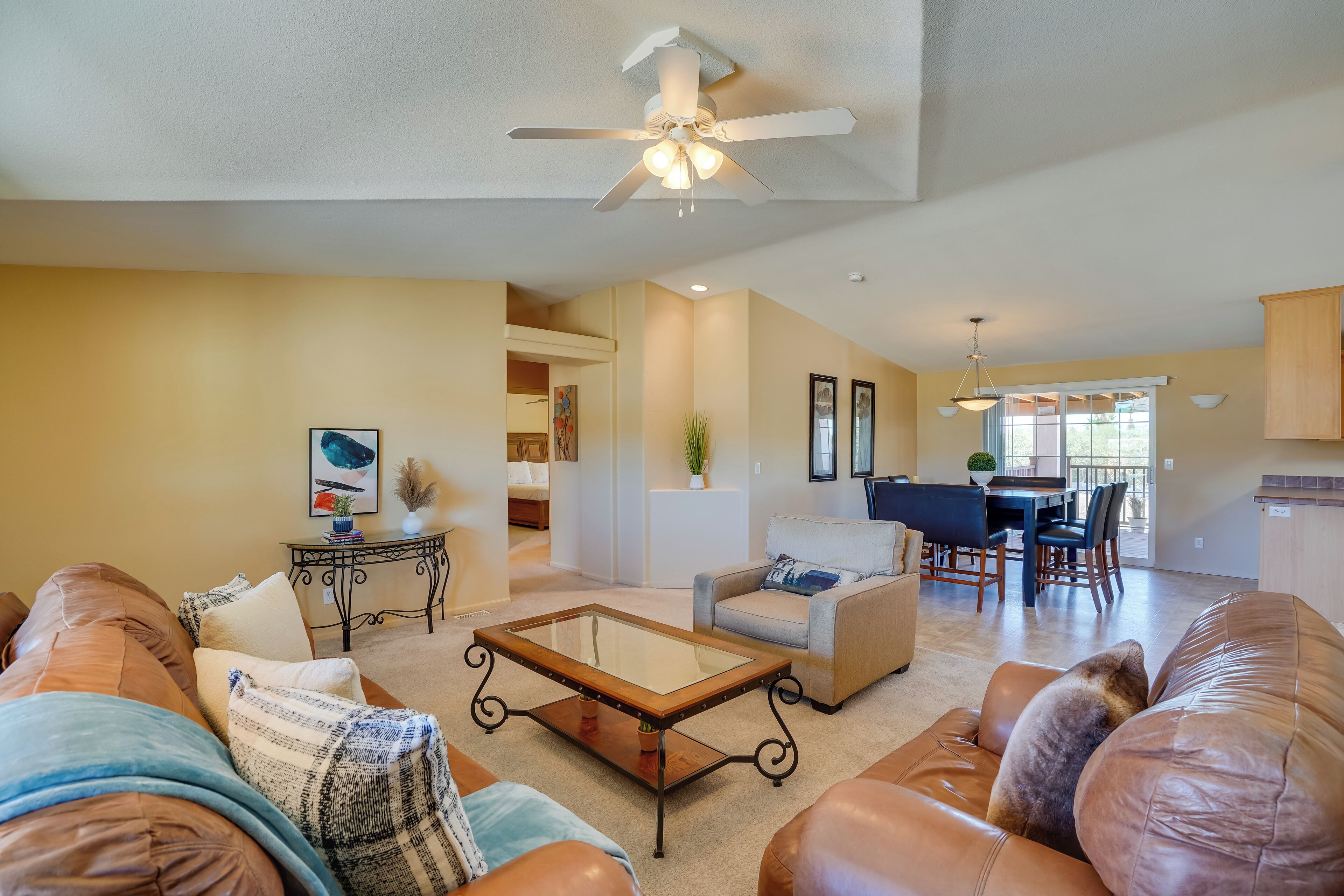 A spacious living room with leather sofas, a glass-top coffee table, and a ceiling fan.