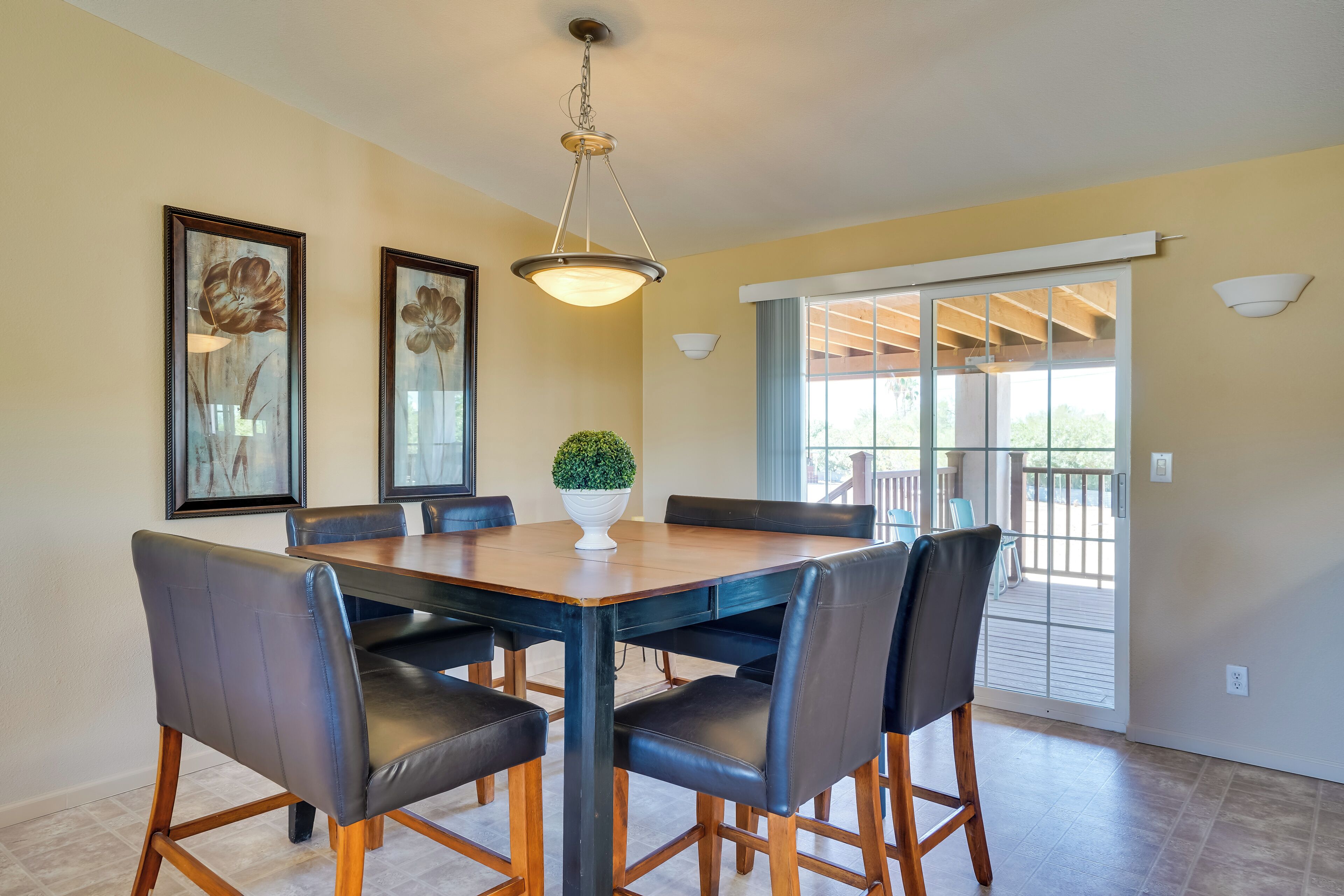 A dining area with a wooden table and black chairs, a hanging light fixture, and a potted plant.