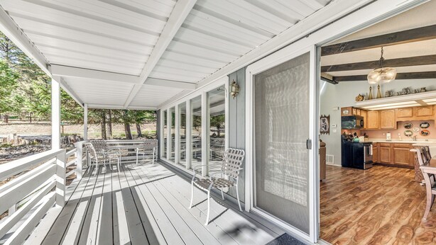 A covered outdoor area with a wooden deck, a seating area with chairs, and a view into a kitchen with wooden cabinets and a hanging light fixture. - Rustic Alto Retreat - Near Hiking, Skiing & More! (Alto)