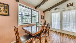 A dining area with a wooden table and chairs, a large window with a view of trees, and a door with frosted glass panels. - Rustic Alto Retreat - Near Hiking, Skiing & More! (Alto)