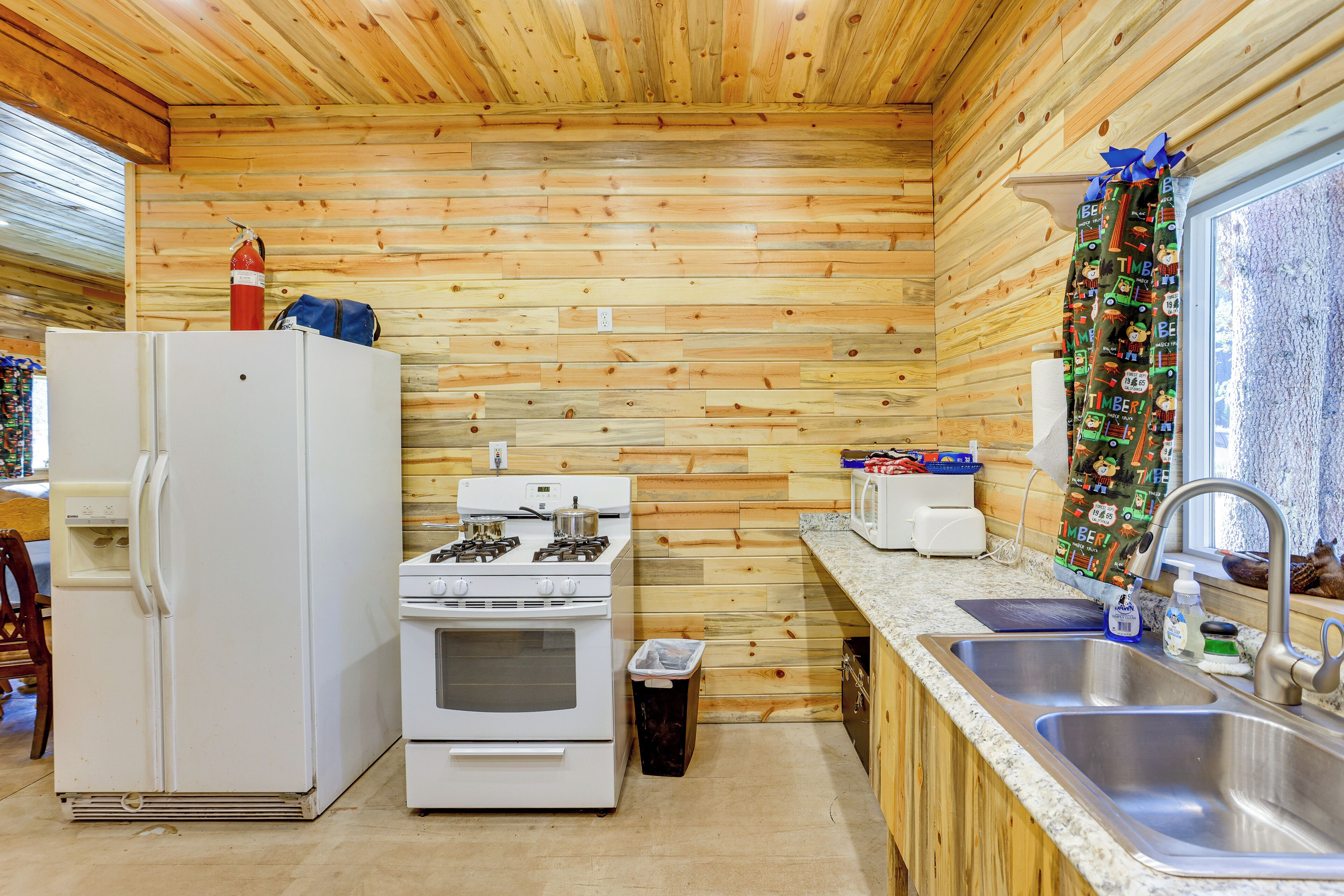 Une cuisine de taille réduite avec des murs en bois, un réfrigérateur, une cuisinière, un four à micro-ondes et un évier.