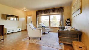 A living room with a wooden floor, two white armchairs, a grey sofa, a white cabinet, and a large window with curtains. - Spacious Canyon Ferry Lake House With Bar & Views! (Helena)