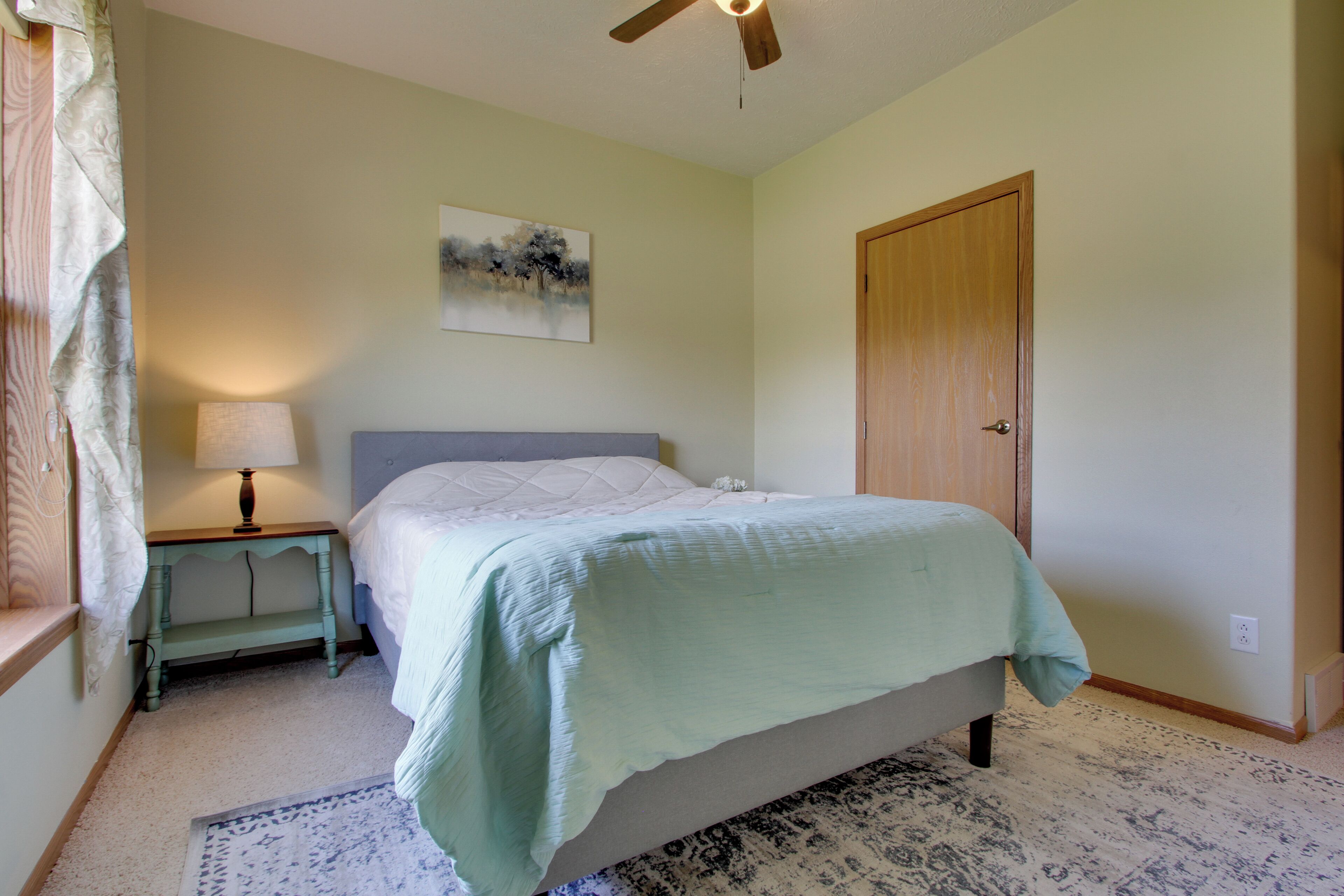 A bedroom with a bed, a nightstand, a lamp, a door, and a painting on the wall.